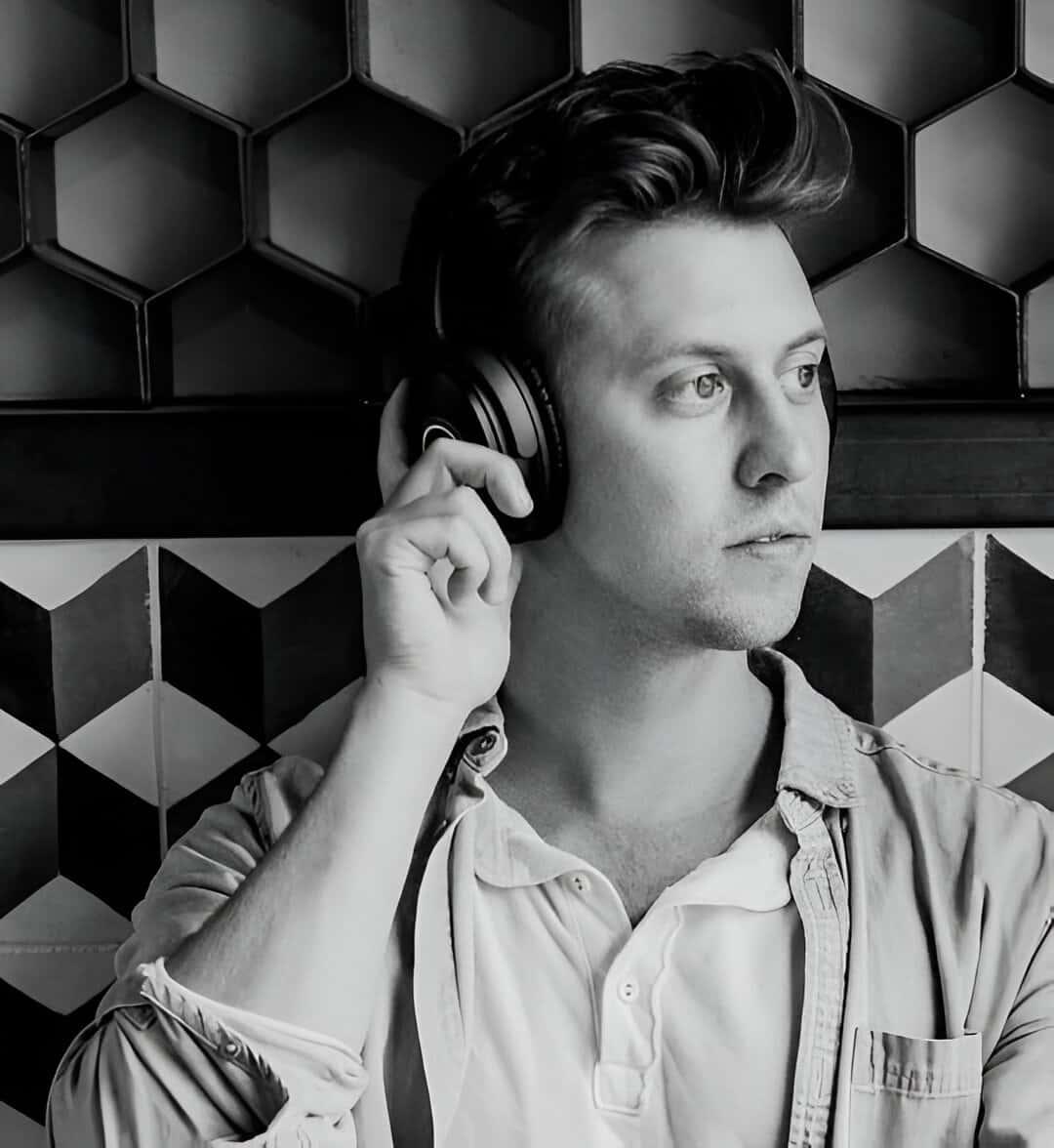 A man enjoying music with sleek headphones against a geometric-patterned backdrop, in a serene black and white setting.