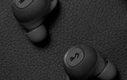 A pair of wireless in-ear earphones, with a dark, textured surface that suggests a premium, matte finish. The ear tips contrast in color, made of a soft silicone material.  The grayscale presentation of the image accentuates the earphones' sophisticated design.