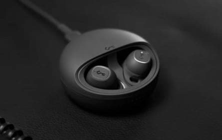 A pair of black in-ear earphones, neatly placed within a small, round case that ensures their safety and portability. The earphones are modern and compact, with a dark, textured surface that gives them a sophisticated appearance. The black case, with its smooth surface texture, appears durable and is designed for convenience
