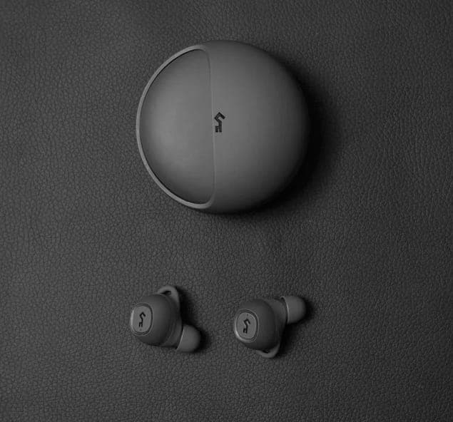 A pair of black wireless earbuds rest next to a small black charging case on a flat black surface. View from the top.