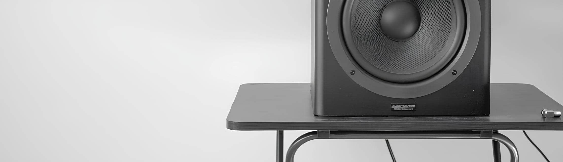 A black ZX7 speaker sitting on a wooden table. The speaker is a rectangular prism with a black, fabric grille on the front. It has a small, silver logo on the bottom right corner of the front grille.