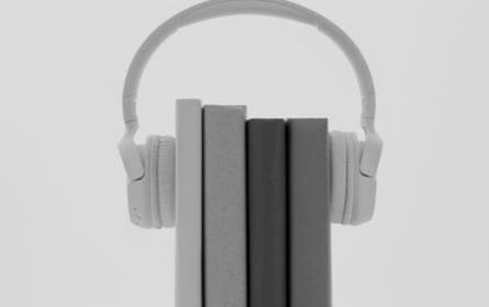 A pair of white over-ear whireless headphones resting on a stack of hardcover books.