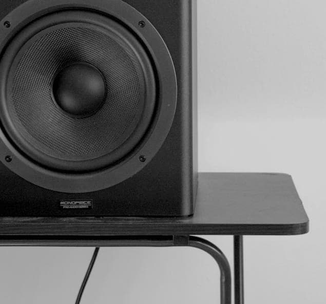 ZX7 speaker in black and white, highlighting its sleek design with a prominent woofer, set against a minimalist wooden table backdrop