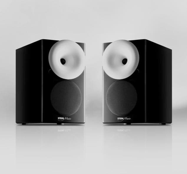 Two sleek black speakers with a white tweeter and dark woofer, placed side by side on a reflective surface.